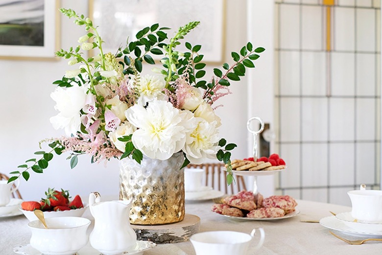 Textured gold-white vase with white and pink flowers on table with white china