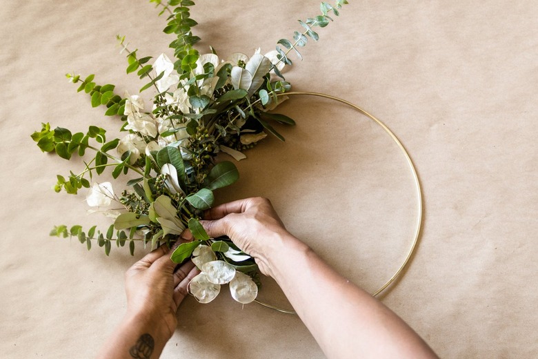 attaching greenery to a brass hoop to make a diy wreath