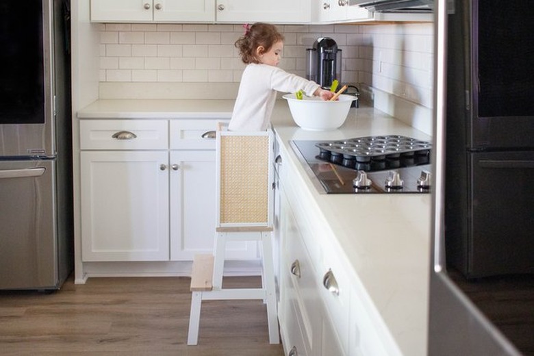Child standing on learning tower in kitchen