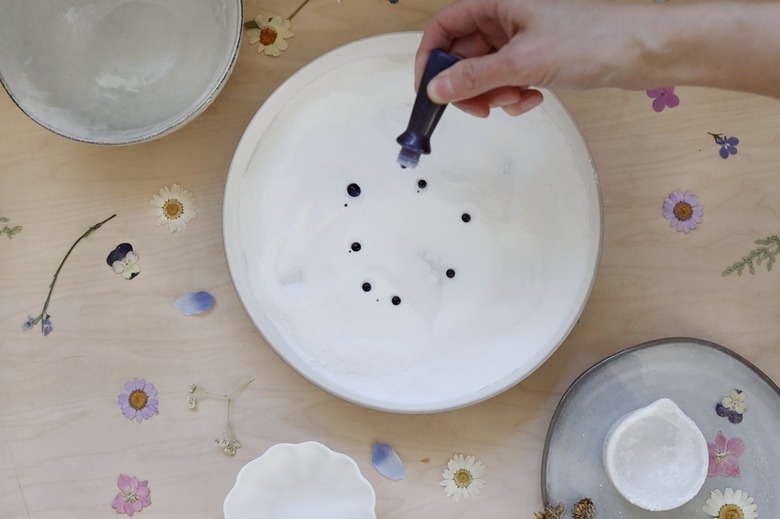 Adding drops of blue plant-based food coloring to powdered mixture in a bowl