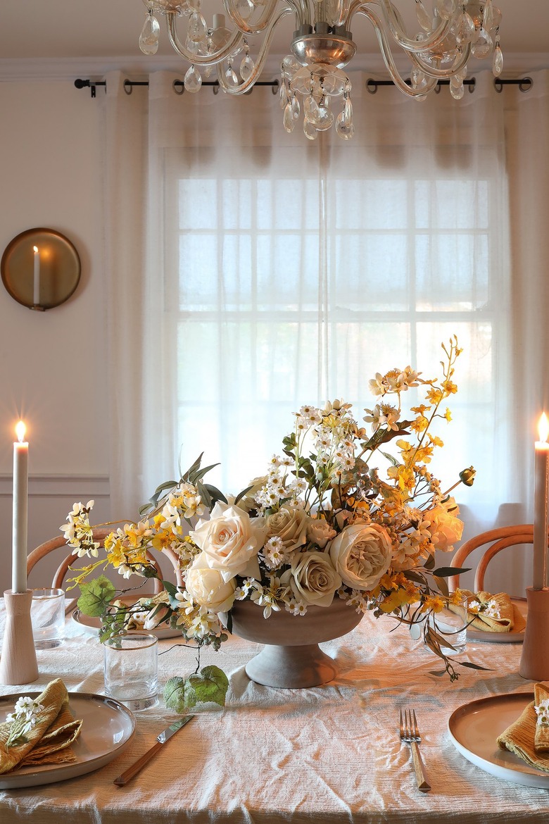 DIY faux spring centerpiece with white and yellow flowers on table with candles