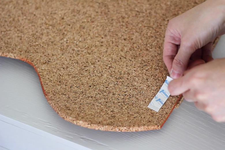 Adhering adhesive strips to back of cork board