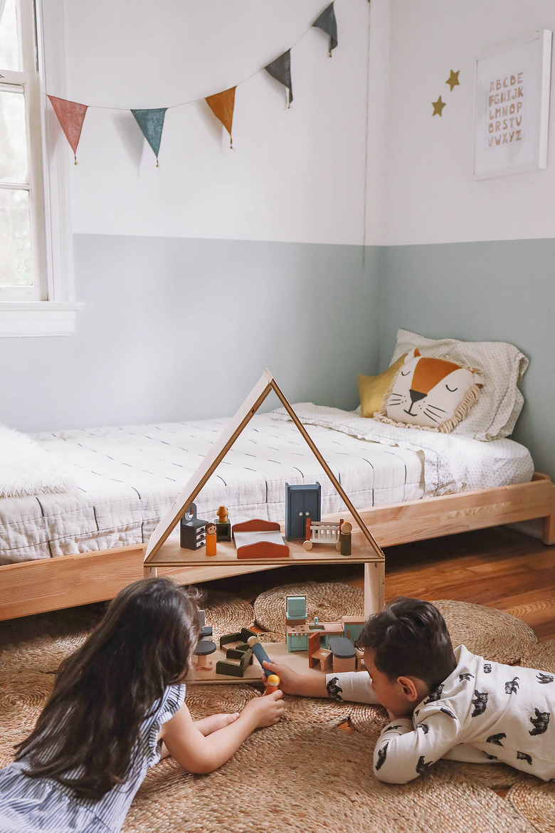 Little girl and boy laying on floor playing with wooden dollhouse in kids' room