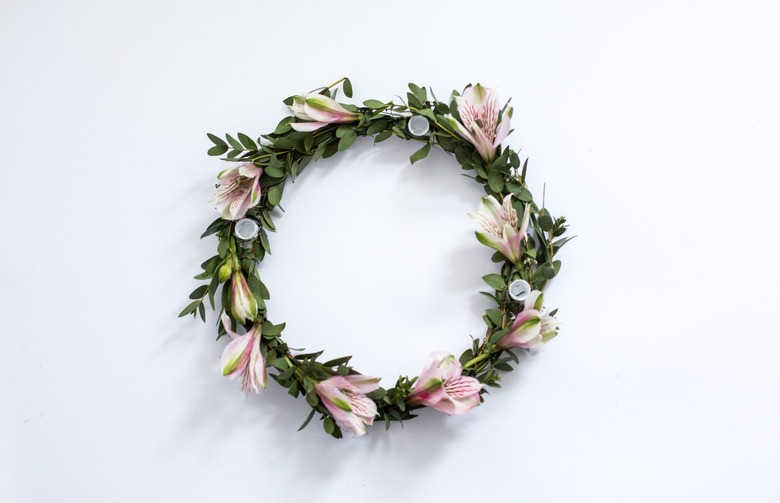 a diy candle holder consisting of greenery and flowers wrapped around a plastic form