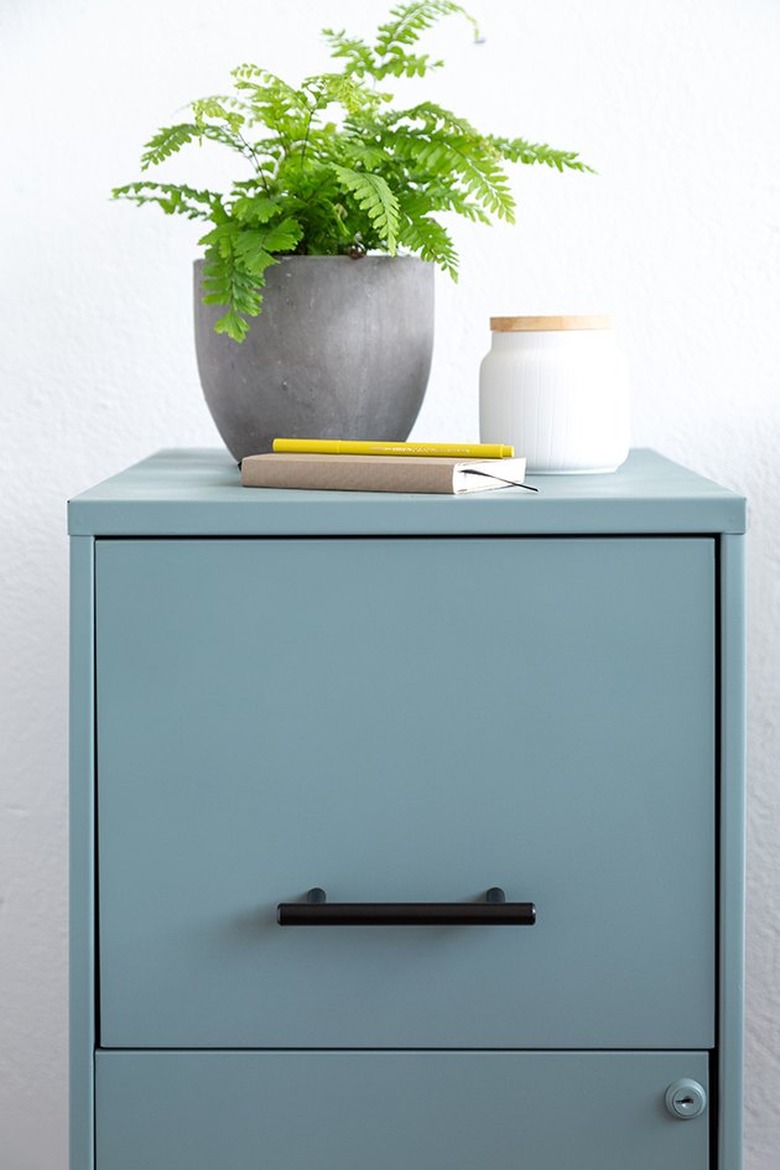 Blue filing cabinet with black handles and green plant.