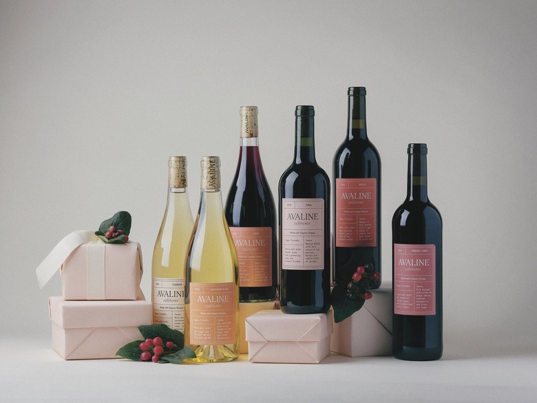 The six wines that make up Avaline's holiday collection rest on an assortment of light pink wrapped gifts. There are holly and berries as well