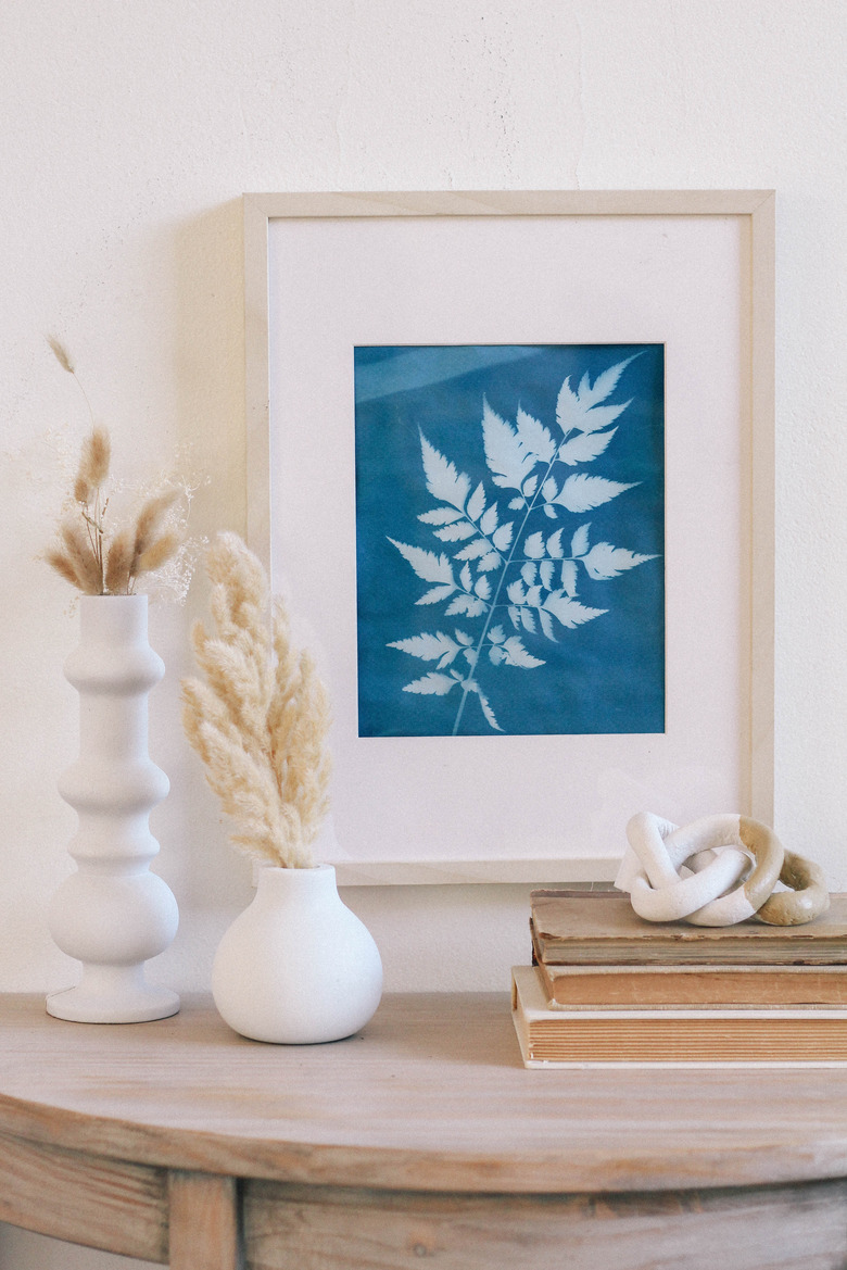 Framed blue sun print hung on wall above table with white vases