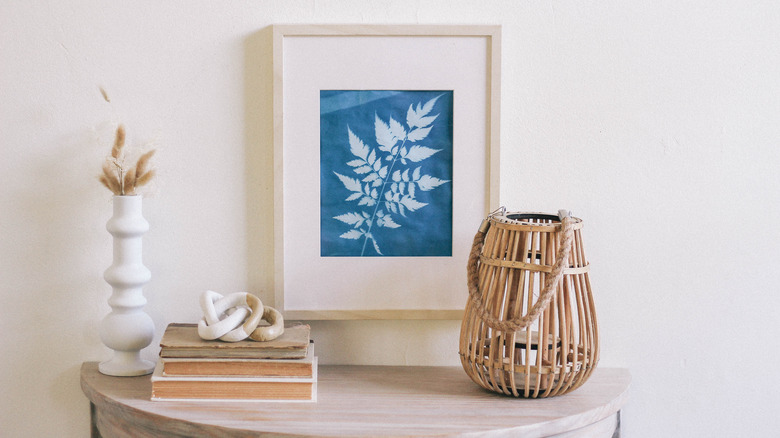 Framed blue sun print hung on wall above table with white vases