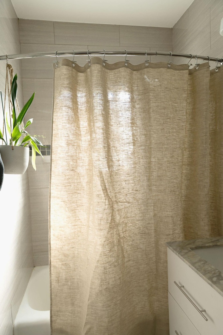 Hemp eco-friendly shower curtain pictured in sunny white bathroom with houseplant on wall