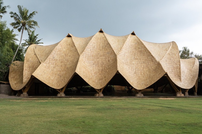 Exterior of a large bamboo building with a sloping rooftop and palm trees on the back