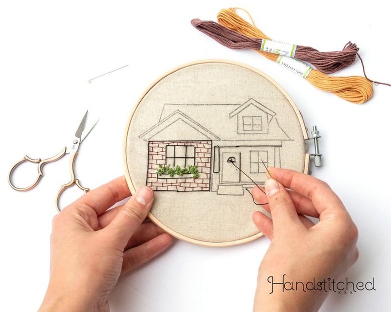 person embroidering a hoop with a pattern of a house