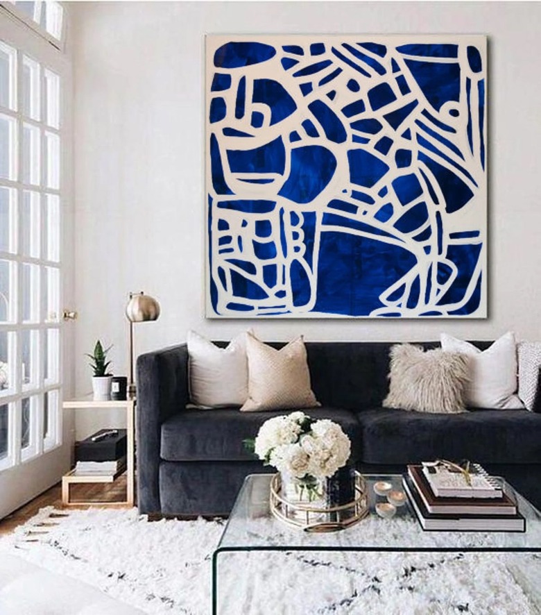 Blue and white painting on a white wall in a room with a navy blue couch