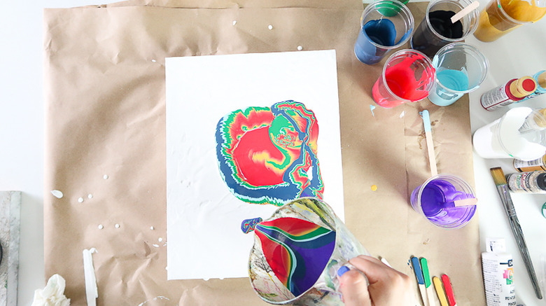 Pouring paint onto canvas from cup.