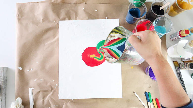 Pouring paint onto canvas from cup.