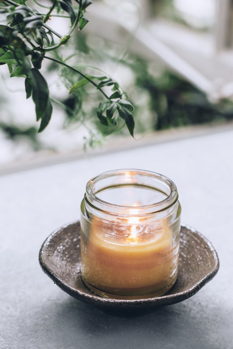 a diy beeswax candle burning in a glass jar on a saucer