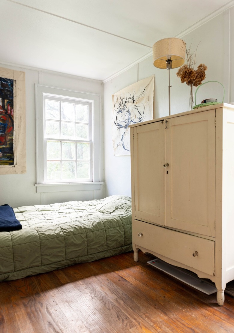 a large off-white vintage armoire towers over a low bed with no frame