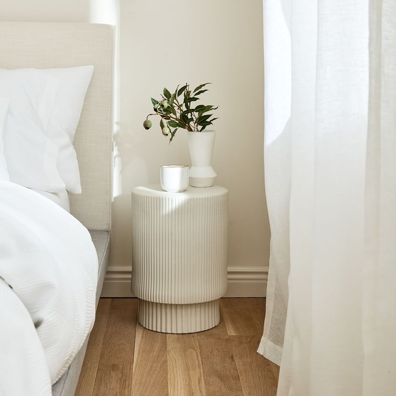 white fluted side table with vases next to bed