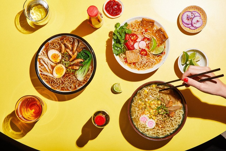 bowls of ramen and food with person holding chopsticks nearby