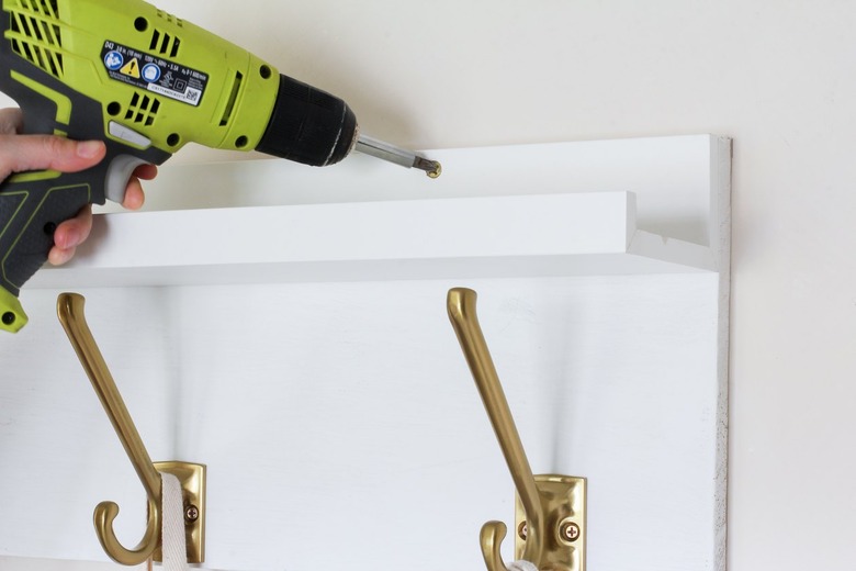 Hand screwing white kitchen wall hangers with gold hooks onto white wall with gold screws