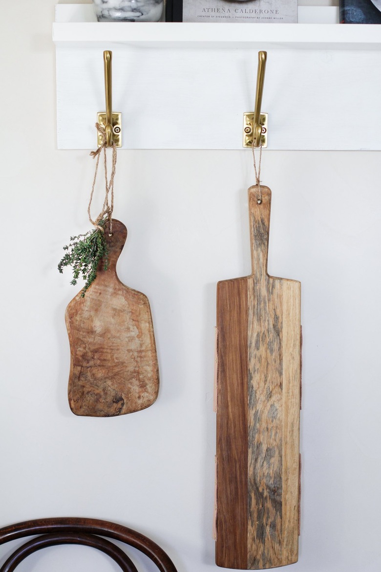 White kitchen wall hangers with gold hooks holding cutting boards against white wall