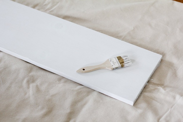White painted board resting on canvas sheet with white paintbrush