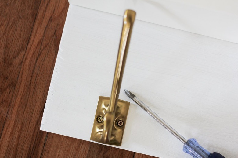 White kitchen wall hangers with gold hooks on wood flooring with screwdriver