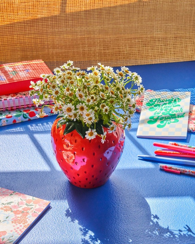 flowers in strawberry shaped vase on table near writing tools