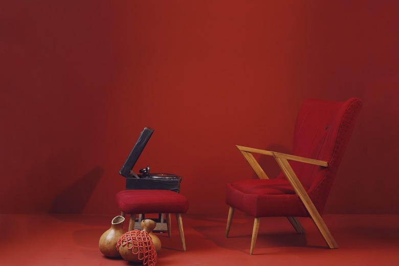 A red armchair and red ottoman in front of a red background next to a record player.