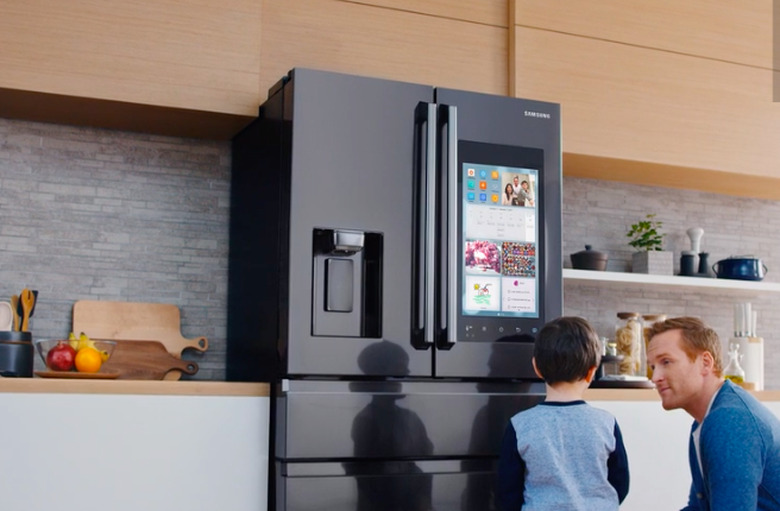 two figures in a kitchen in front of a smart refrigerator with a screen