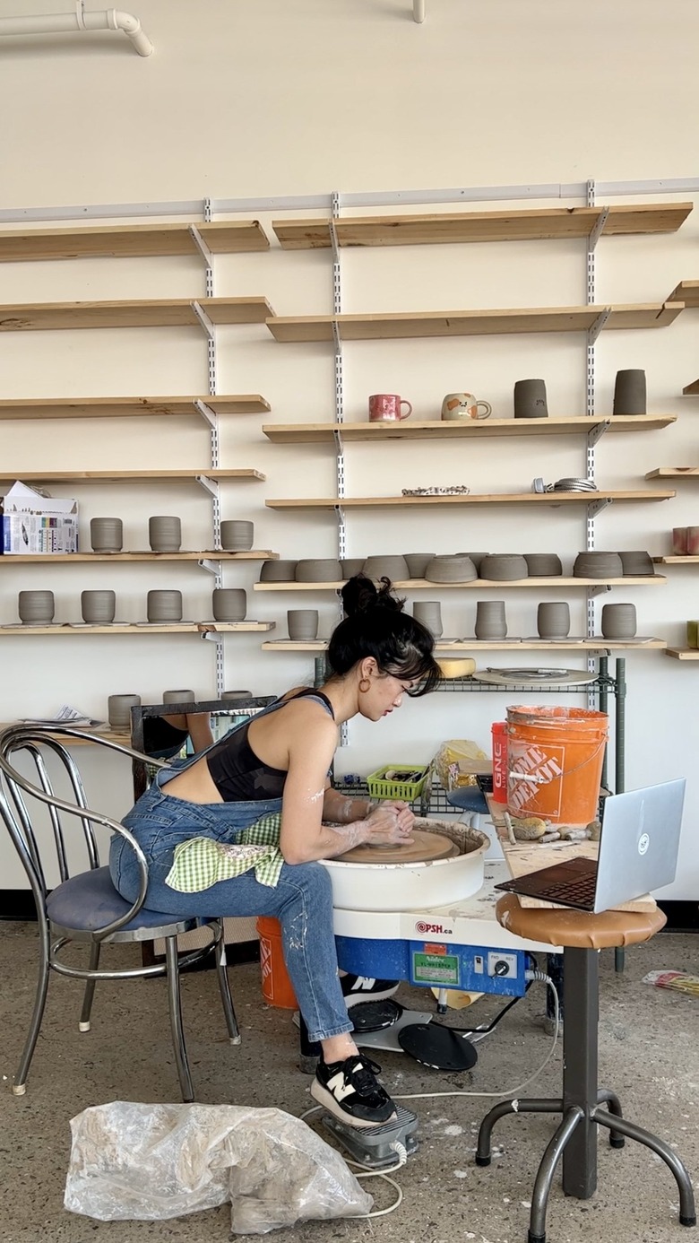 person sitting near shelves at a pottery wheel