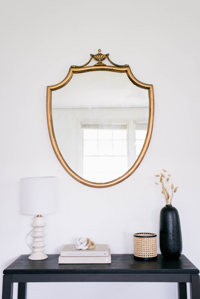 DIY gold gilt mirror hanging on wall above black table with lamp