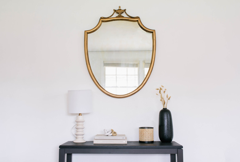 DIY gilded mirror hanging on wall above black table with lamp
