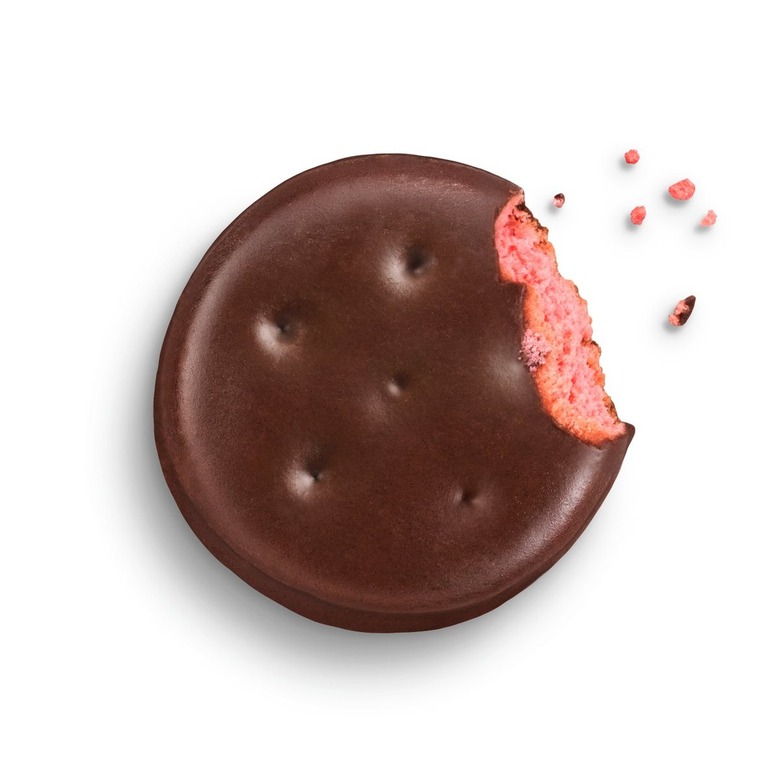 A Raspberry Rally Girl Scout Cookie with a bite taken out of it. It's round and covered with chocolate with pink filling.