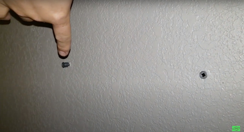 silver screws in white wall with finger pointing at one