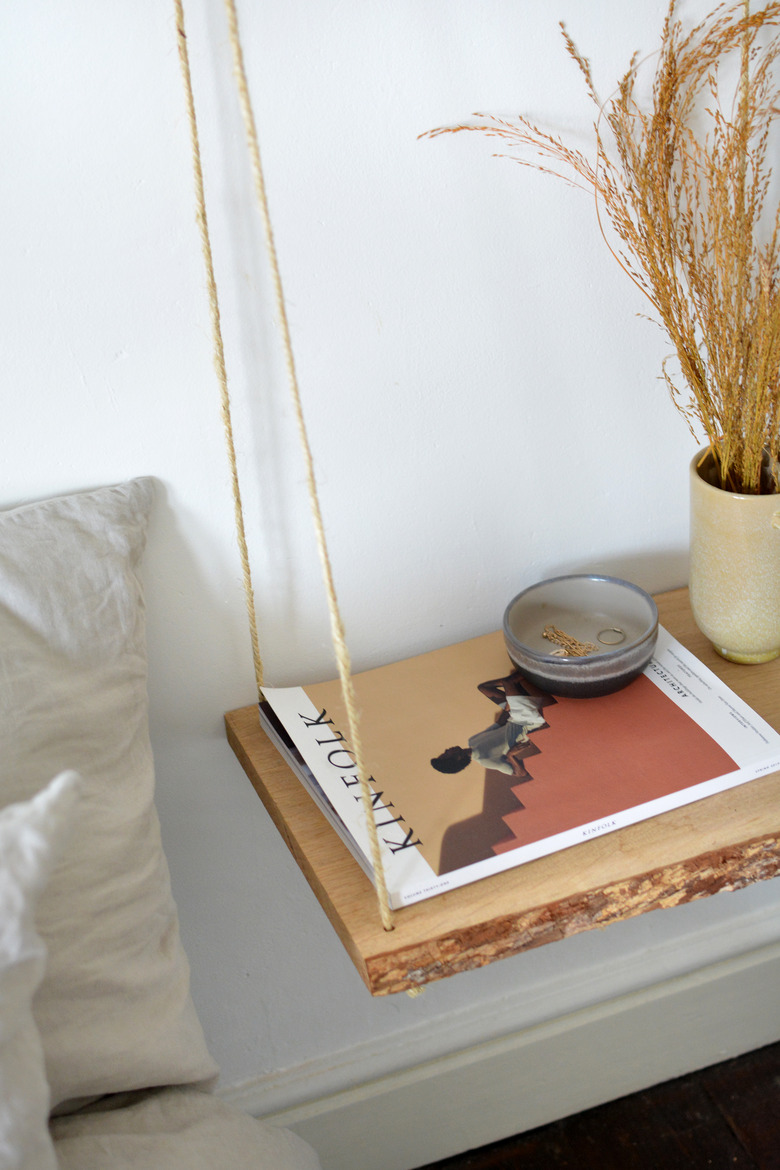 Wooden shelf suspended from rope with a magazine and grey bowl and beige vase.