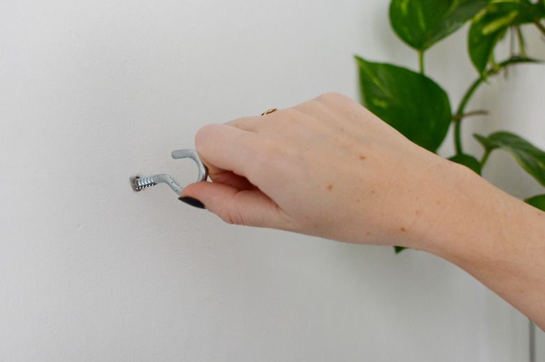 Hand twisting a metal silver hook into a hole in a white wall.