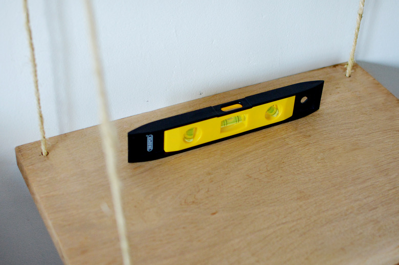 A piece of wood hangng from natural rope with a black and yellow spirit level on top