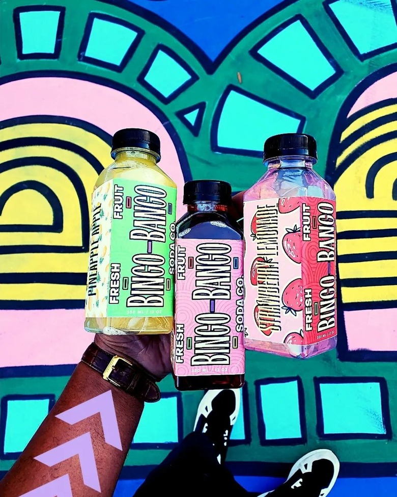 Bingo-Bango Fresh Fruit Soda Co. soda bottles in front of colorful geometric mural.