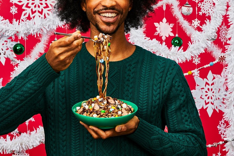 A black man in a green cable knit sweater smiles and holds a bowl of Buddy the Elf spaghetti in one hand