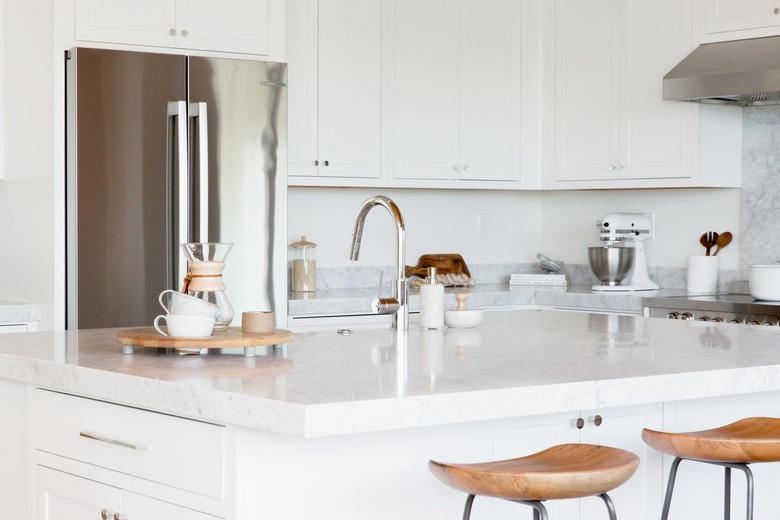 White kitchen island with a marble countertop. Two bar stools with wooden seats and metal legs in fron of it. On the countertop