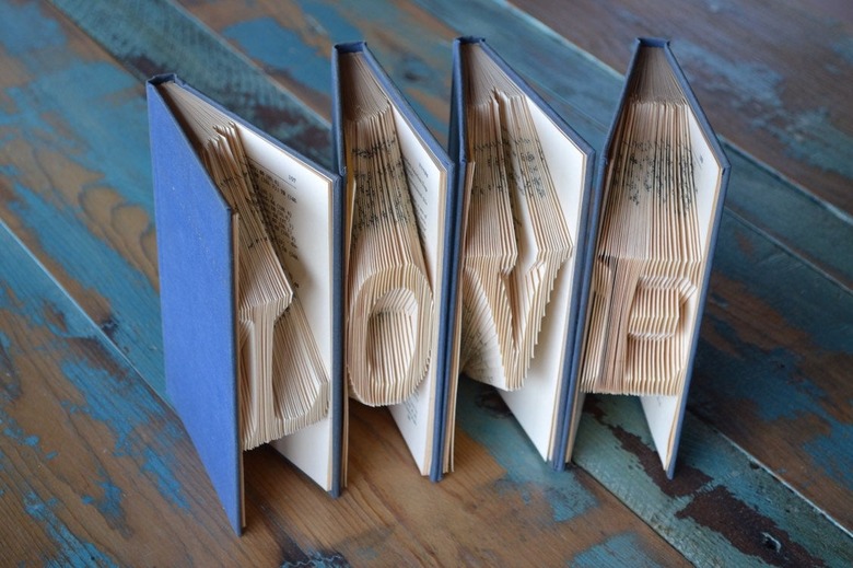 Book sculpture of four books with blue covers and folded paper spelling Love