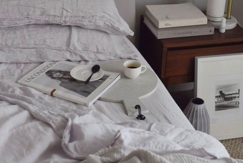 Unmade bed with white linens and a coffee cup