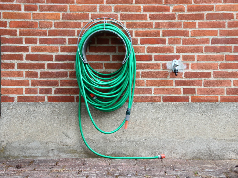 Green Garden Water Hose mounted on Red Brickwall