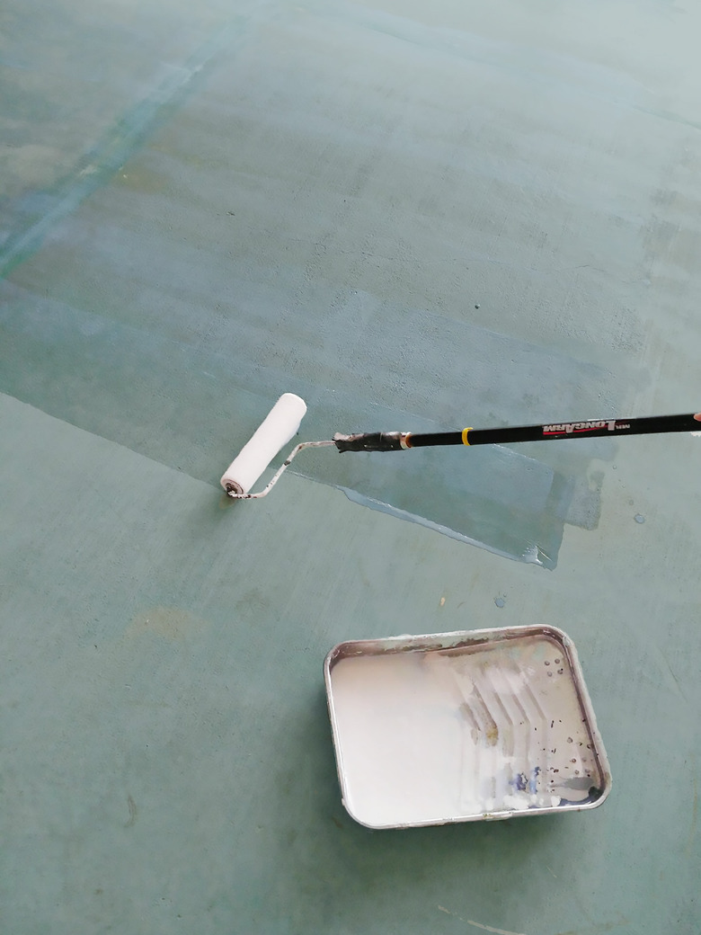 A paint roller going over concrete floor with sealant.