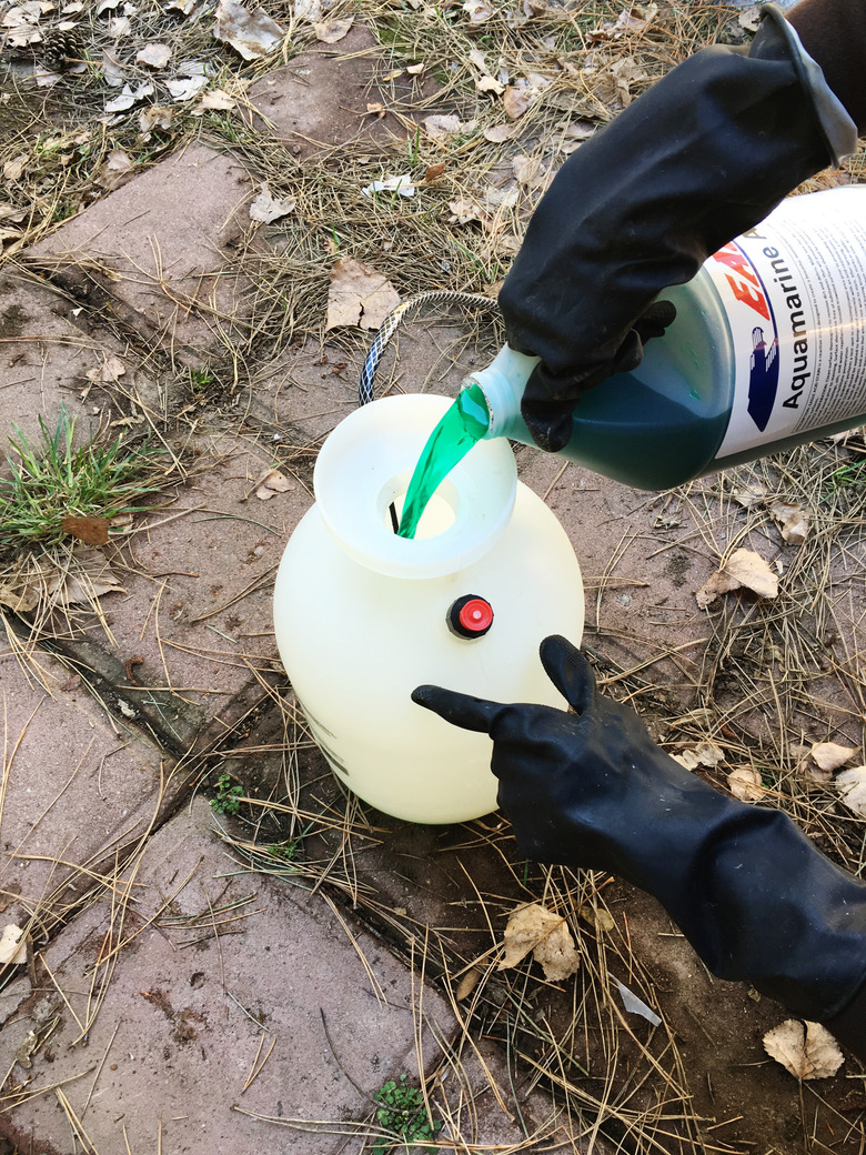 Person with black rubber gloves pouring green acid into a pump sprayer.