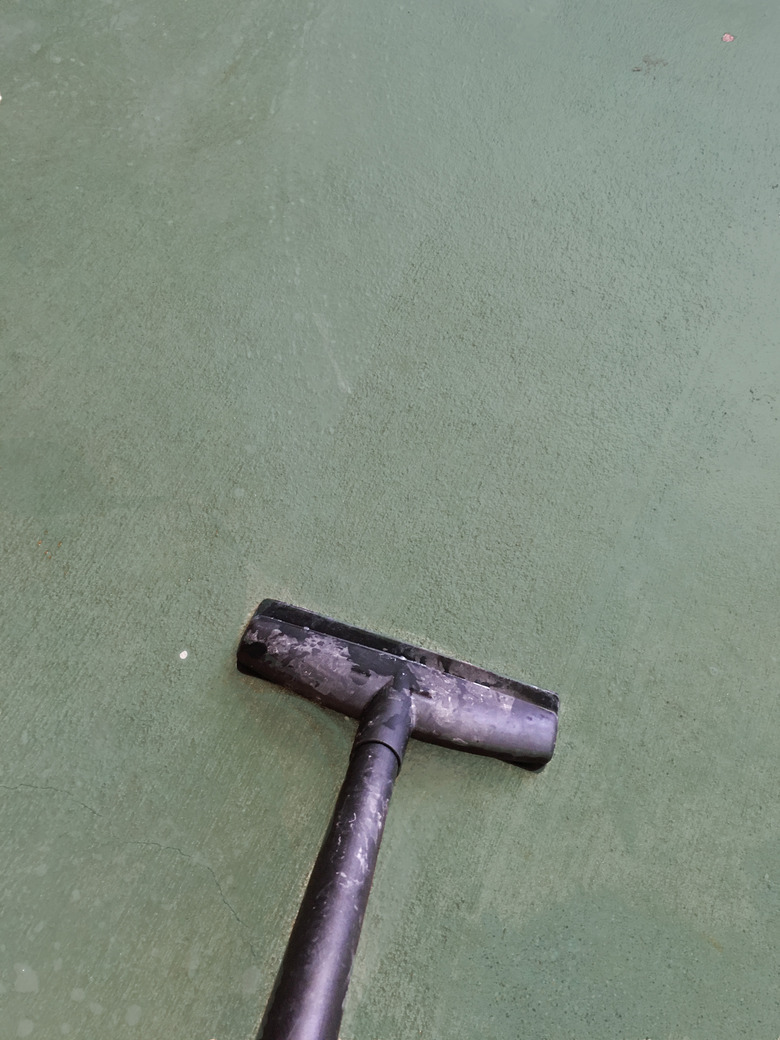 A black vacuum on a green concrete floor.