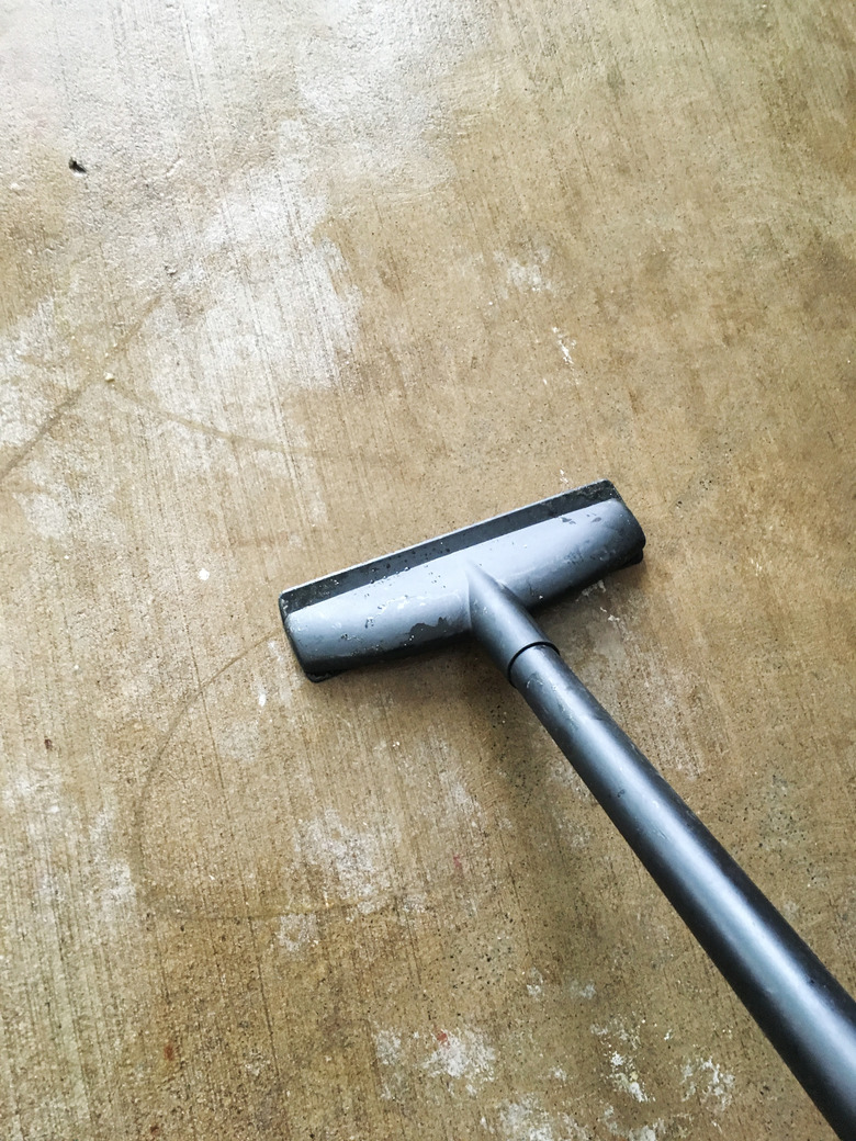 A black vacuum on a concrete floor.