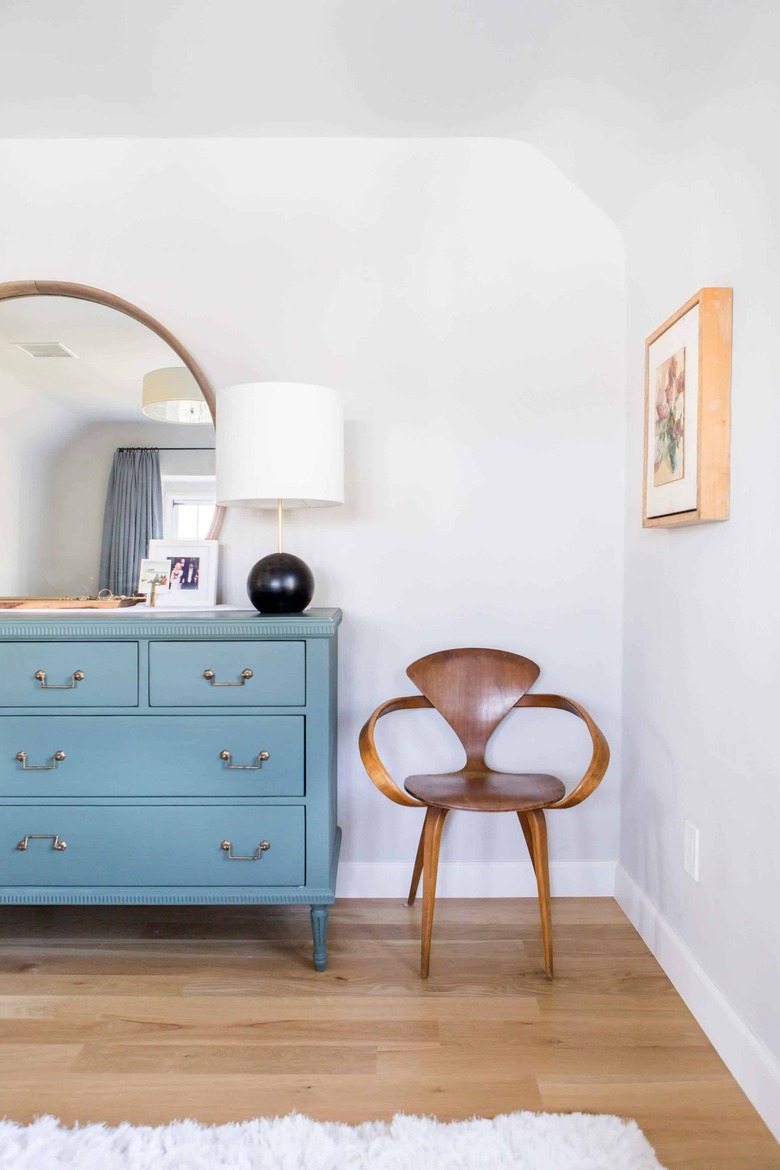 A white bedroom with a blue dresser with a large mirror