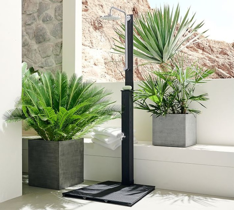 A freestanding outdoor shower near concrete planters in a backyard alcove