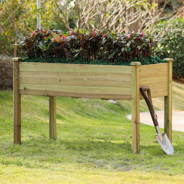 An elevated wooden planter with a shovel leaning against it